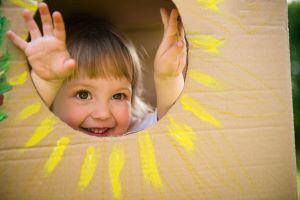 I little girl peeks through a sunshine hole in a cardboard box.