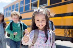 A little girl gives the "thumbs up" sign as she and others prepare to get on a school bus.