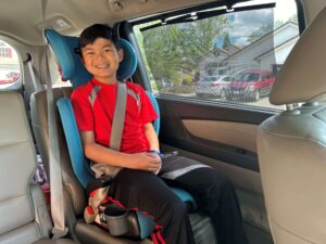 A young boy sitting in a booster seat flashes a warm smile.