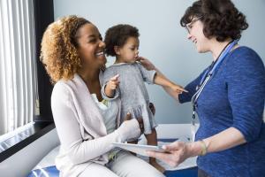 This is a photo of a mother with her child undergoing a checkup at a pediatric care center. The doctor is reviewing the child's chart.