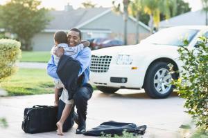 This is a photo of a little boy greeting his dad with a hug in the driveway.